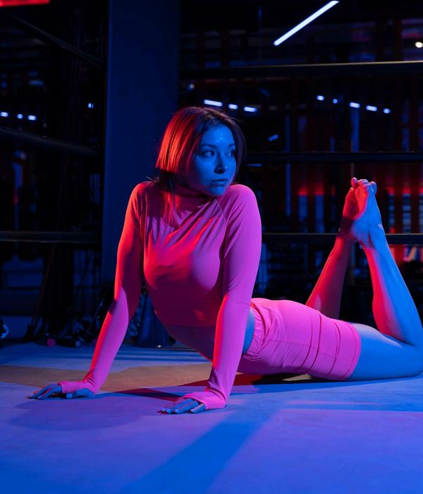 Woman in a calm yoga pose in a dark room with pink neon light.